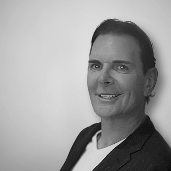 Black and white portrait of a smiling man in a blazer and white shirt.