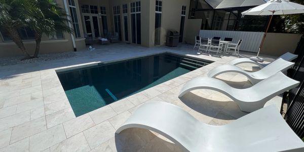 Modern backyard pool with white lounge chairs and umbrellas on a sunny day.