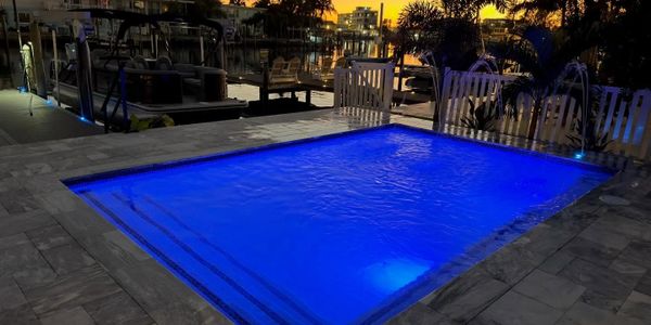 A glowing blue pool at dusk near a waterfront dock.