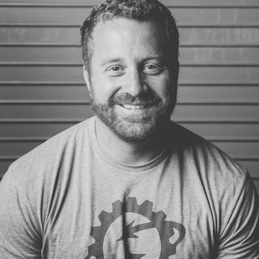 Smiling man with curly hair and beard wearing a graphic t-shirt.