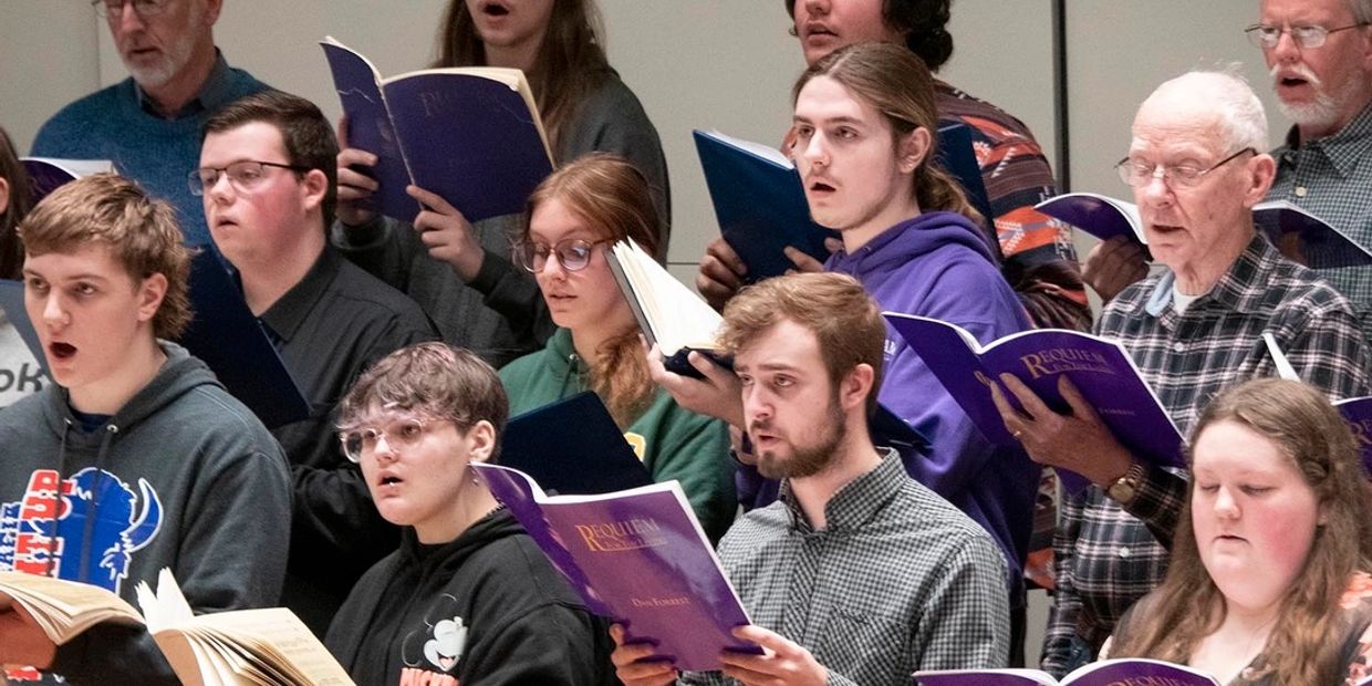 A diverse choir group rehearsing with songbooks in hand, singing passionately.