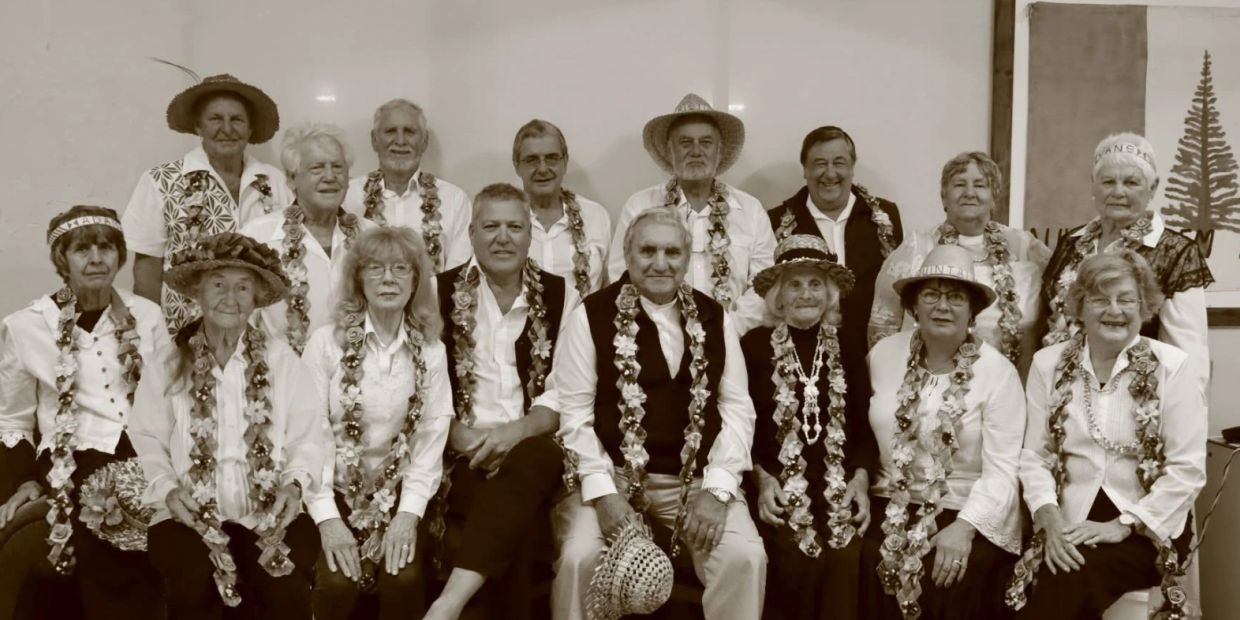 Group of senior people wearing leis and hats, posing for a photo.