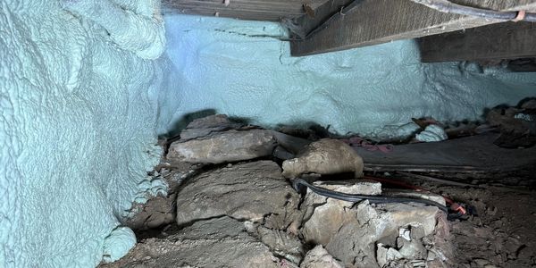 Freshly sprayed foam insulation in a basement crawl space with exposed dirt and rocks.