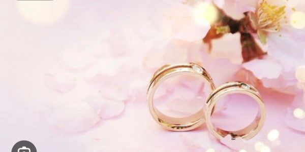 Two gold wedding rings on soft pink flower petals with bokeh lights.