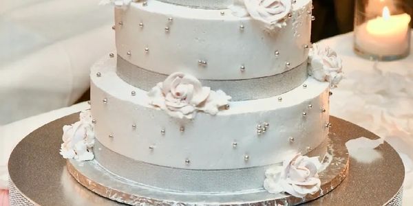 Elegant three-tier white wedding cake adorned with white roses and silver beads.
