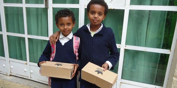 Two young Ethiopian children each holding a box containing a new pair of shoes