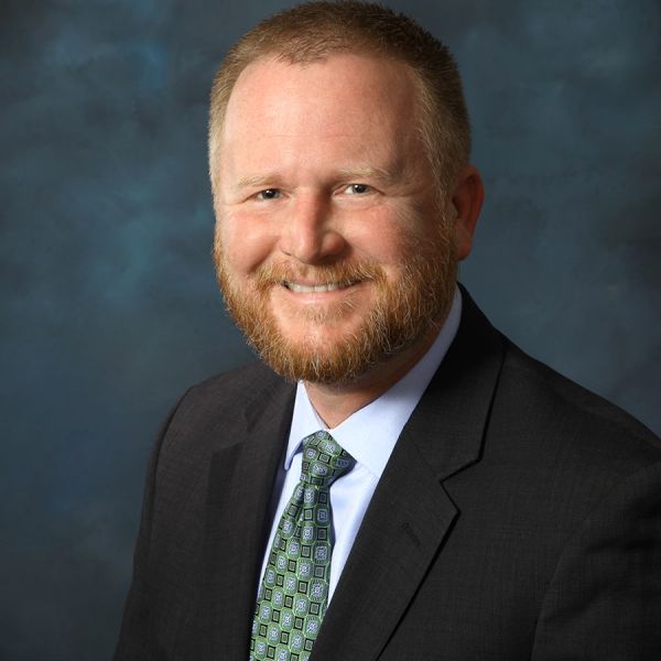 Smiling man in a suit with a patterned tie against a blue backdrop.
