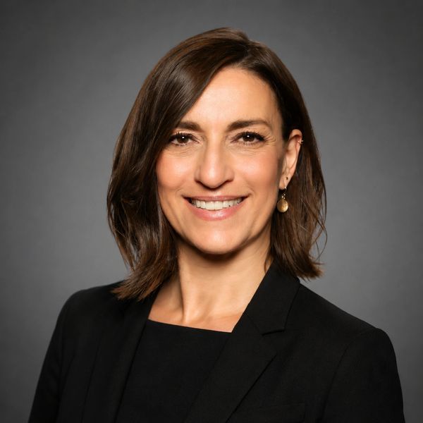 Professional woman smiling in black blazer against gray background.