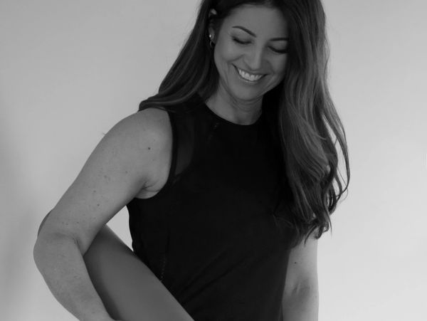 Smiling woman holding a rolled-up yoga mat.