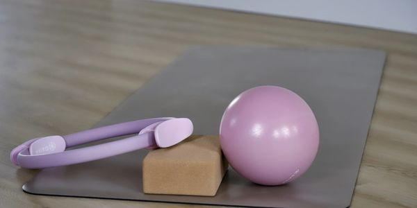 Pilates equipment on a gray mat including a pink ball, ring, and cork block.
