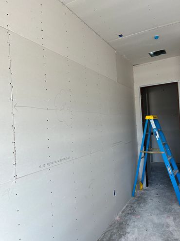 Newly installed drywall with a blue ladder on a construction site.