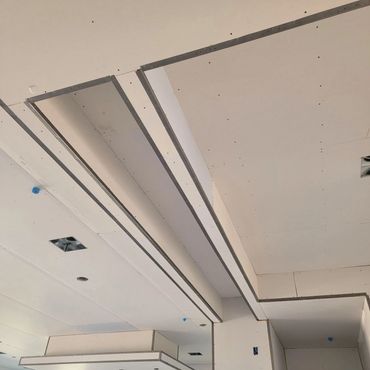 Drywall installation on a ceiling with recessed lighting spaces and metal framing.