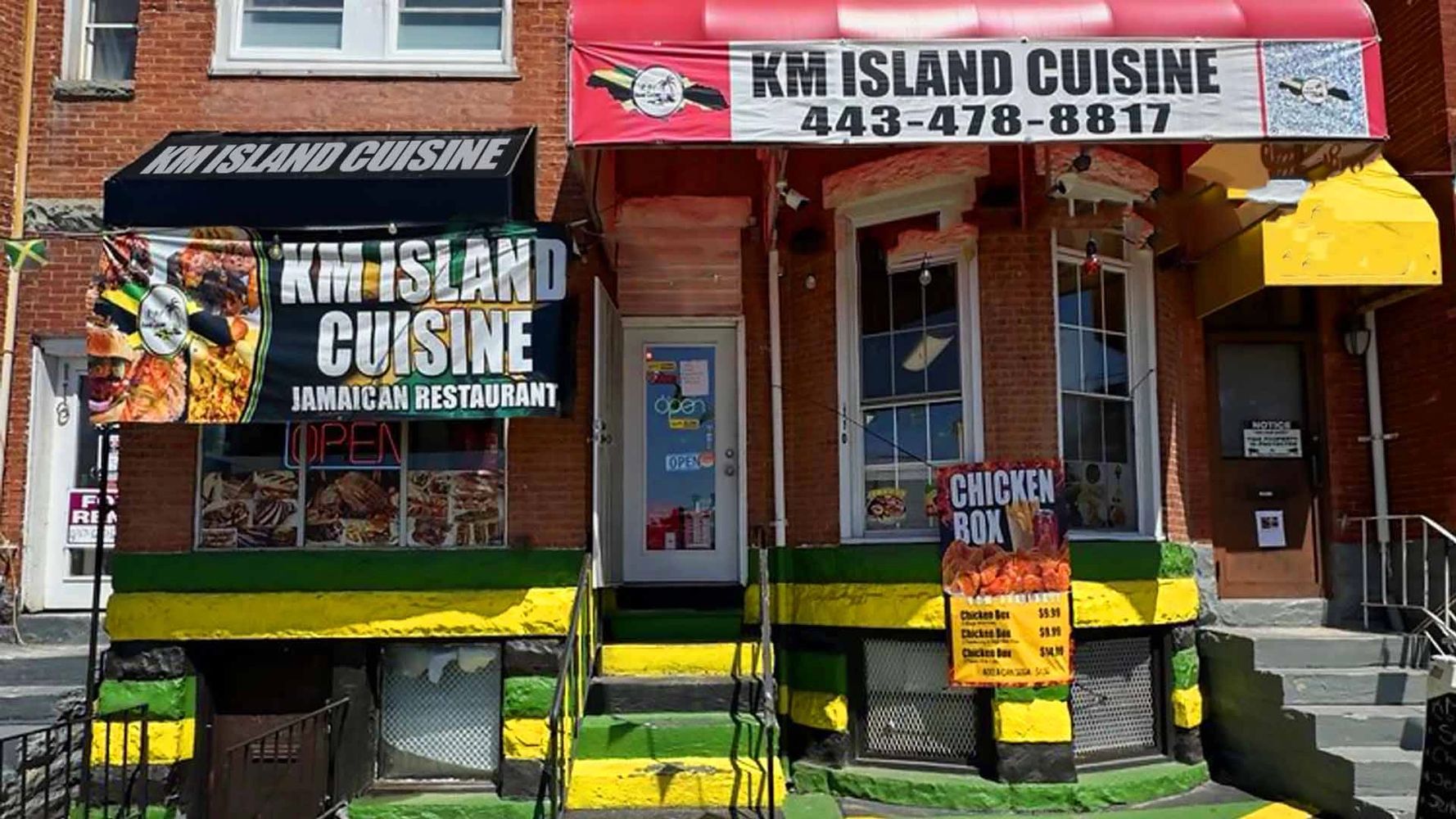 Front view of KM Island Cuisine, a Jamaican restaurant with colorful green, yellow, and black painted steps.