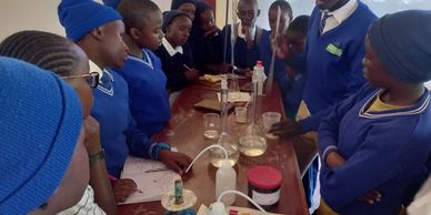 Students in blue uniforms attentively observe a chemistry experiment in a classroom.