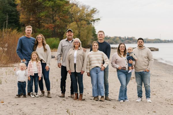 A multi-generation family posing together on a beach with trees in autumn.