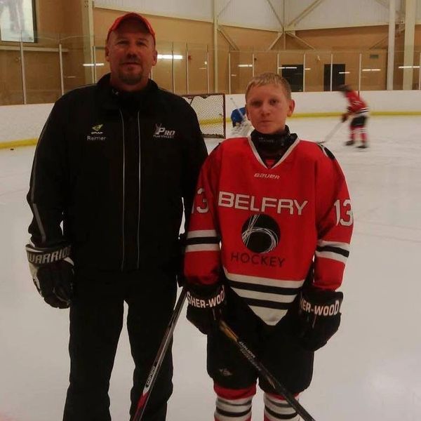A hockey coach and player posing together on an ice rink.