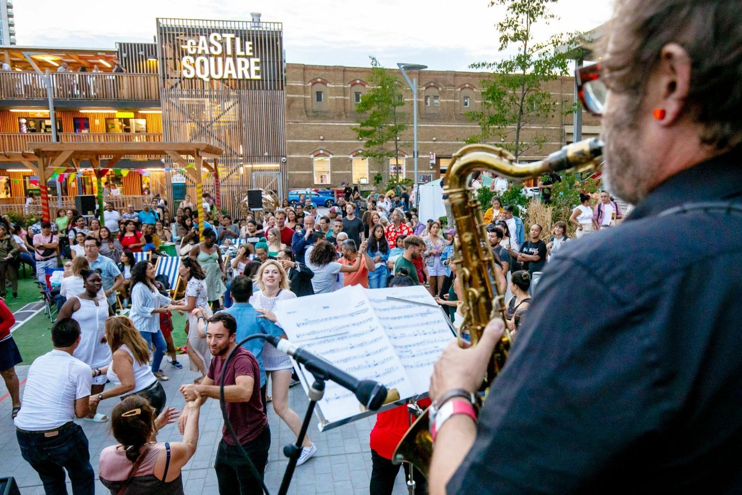 A man playing a saxaophone for a crowd of dancing people in Castle Square
