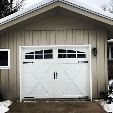 White barn-style garage door on a beige house with snow on roof and ground.