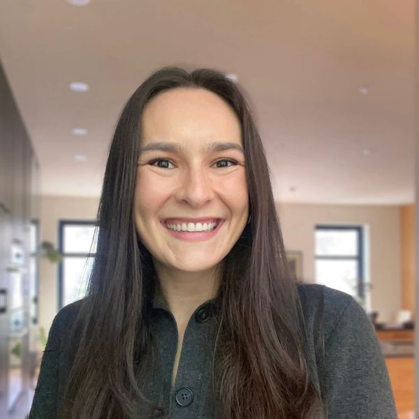 Jeune femme souriante aux longs cheveux bruns dans un intérieur lumineux.