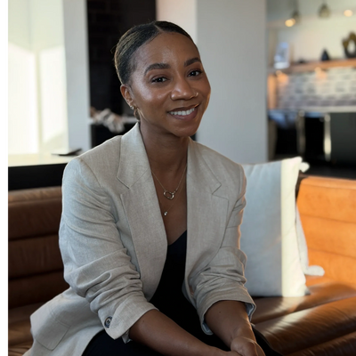 A woman in a beige blazer smiling while sitting indoors.