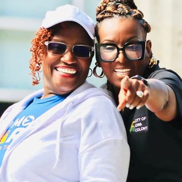 Two women smiling and enjoying a sunny day, one pointing towards the camera.