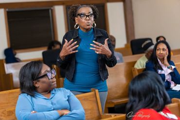 Woman passionately speaking to a seated audience in a meeting room.