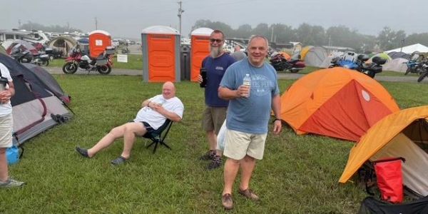 A group of men at a camping site with tents and portable toilets.