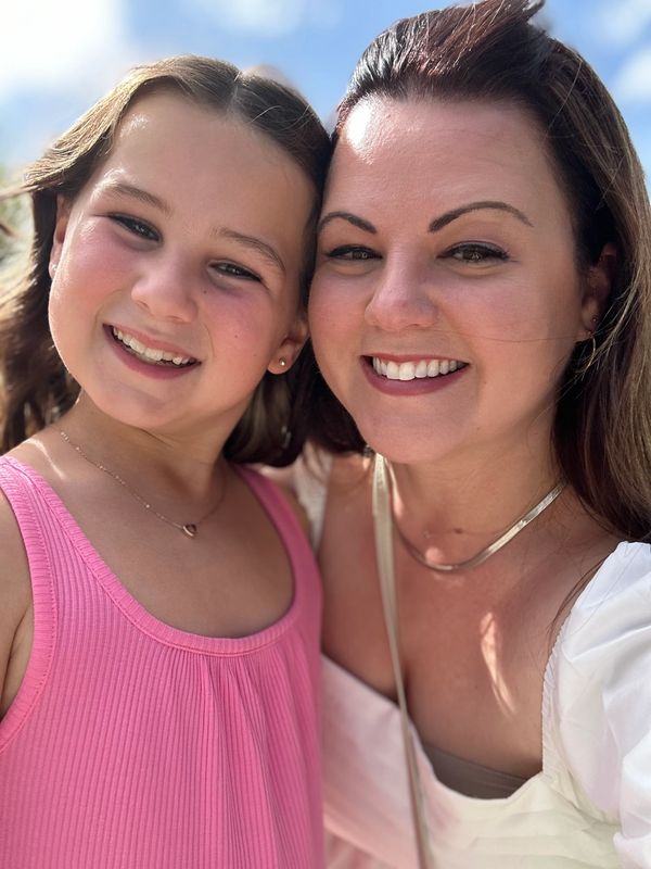 Smiling woman and girl taking a sunny selfie outdoors.