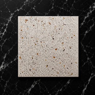 Square terrazzo tile with beige and brown chips on black marble background.
