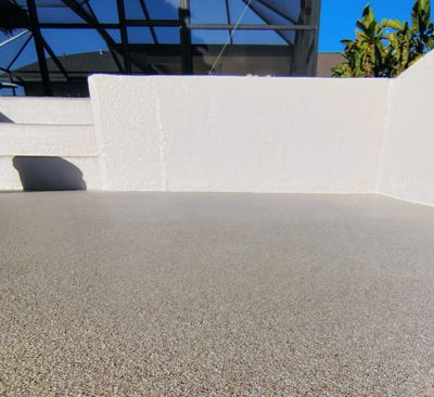 Empty outdoor patio area with textured flooring and white walls under a clear blue sky.