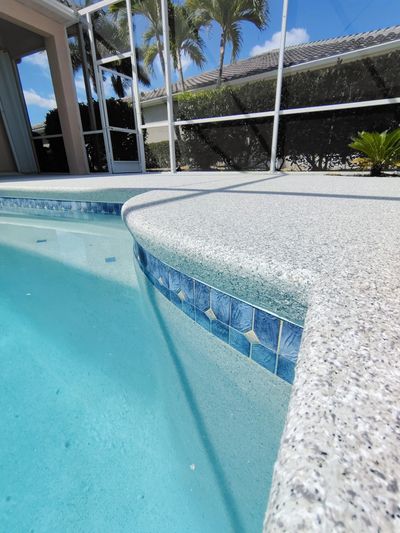 Close-up of a pool edge with blue tiles and clear water under a sunny sky.