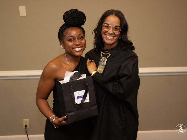 Two women smiling, one holding a gift bag at an indoor event.