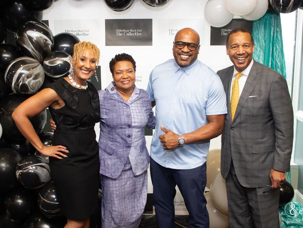 Four people smiling at an event with black and white balloons and a branded backdrop.