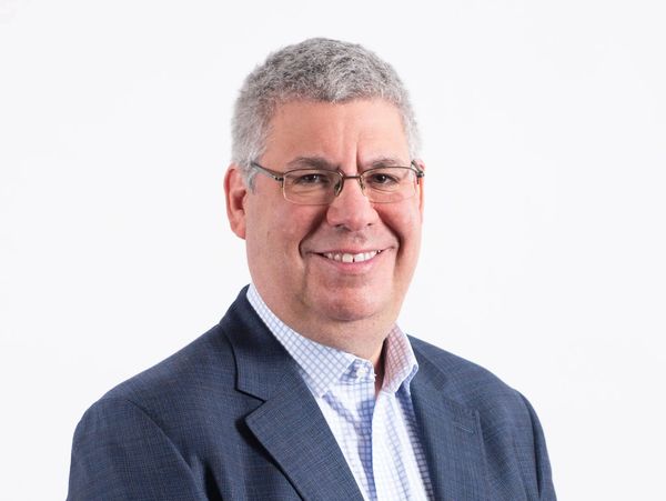 Smiling man in glasses and a blue suit jacket against a white background.