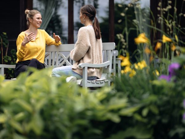 Zwei Frauen sitzen und unterhalten sich auf einer Bank im Garten.