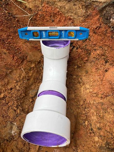 A white PVC pipe with purple primer inside, placed on soil with a blue level tool on top.