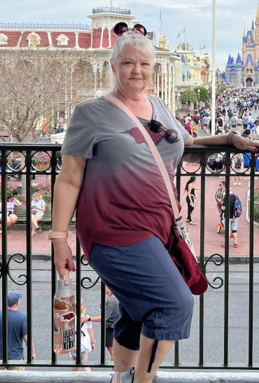 Woman posing with castle and crowd in the background at a theme park.