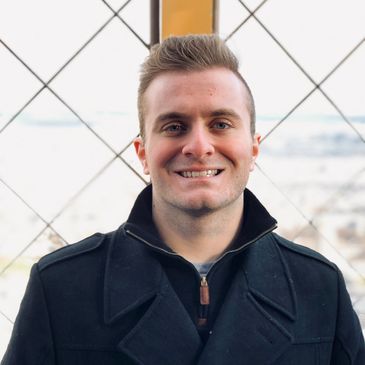 Smiling man in a black coat outdoors.