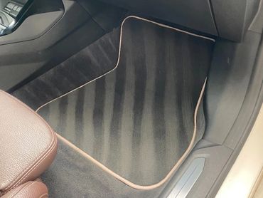 Clean black car floor mat with beige trim inside a BMW.