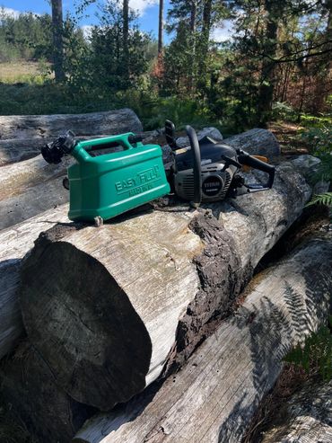 Easyfill no-spill jerry can next to a chainsaw on logs, designed for safe refuelling