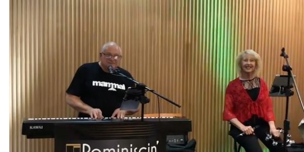 A man playing the piano while another woman stands behind him.