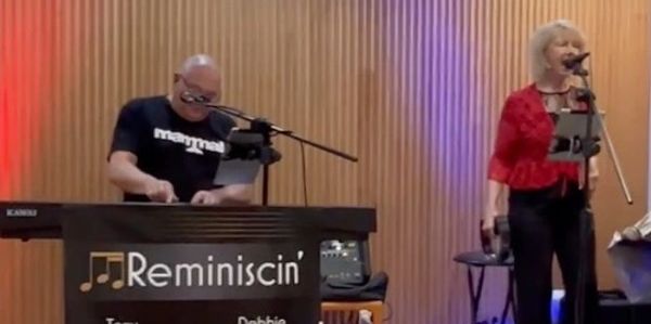 A man and woman singing at a piano.