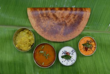 Chettinad Tanjore Masala dosa with fsambar and chutneys served on a banana leaf.