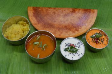 Famous Tanjore Murugan Masala Dosa with chutneys and sambar on banana leaf.