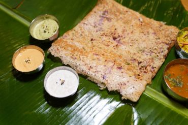 Onion Rava dosa served with chutneys and sambar on a banana leaf.