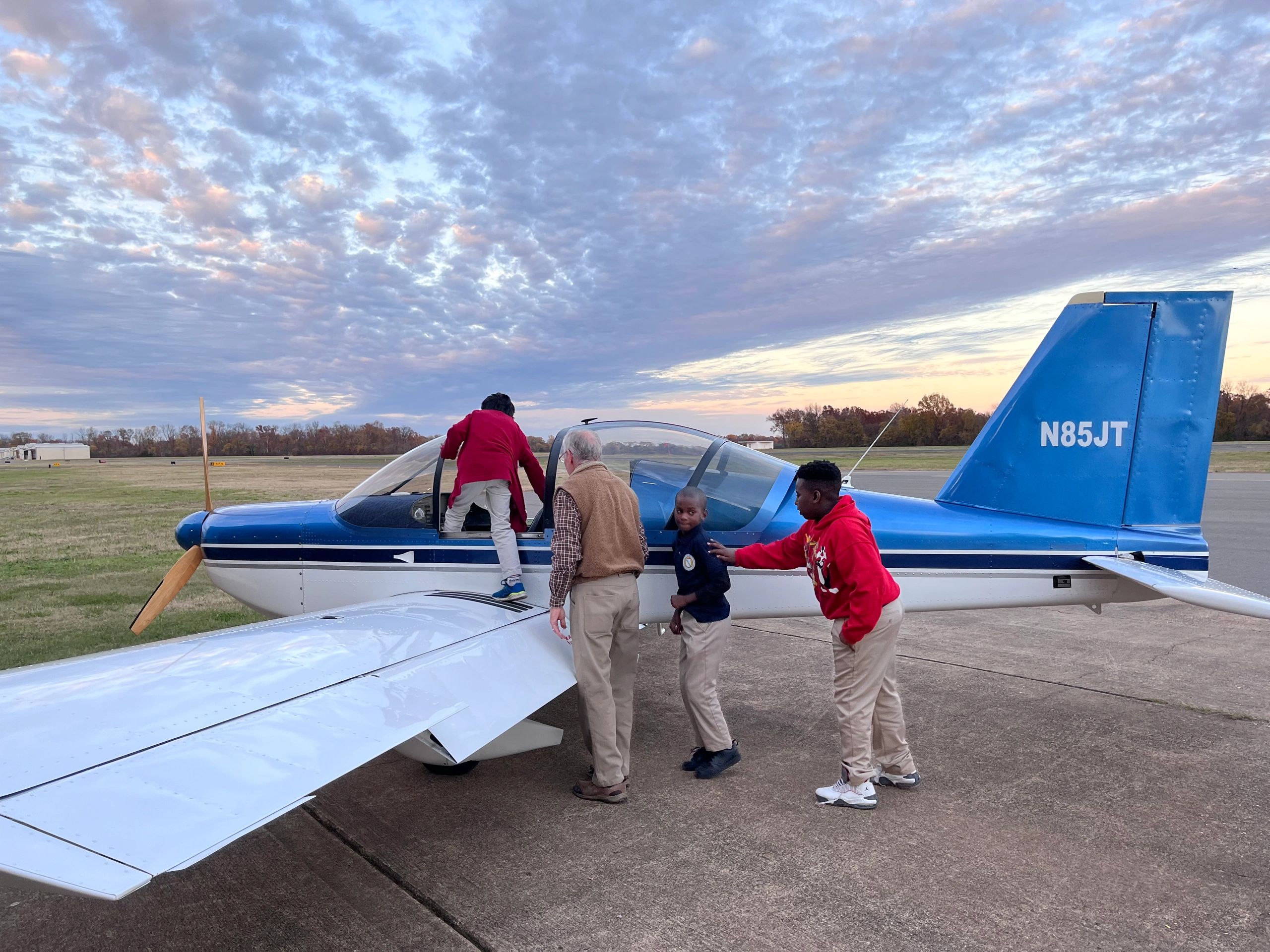 Pilot helping youth climb into a propeller plane to sit in.