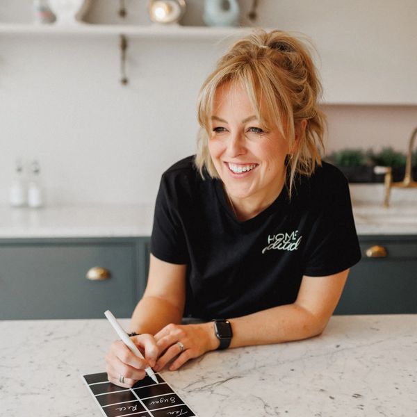Smiling woman writing on a small chalkboard in a modern kitchen.