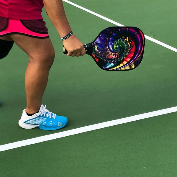 Player holding a colorful pickleball paddle on a court.