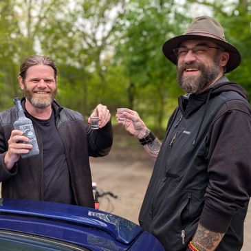 Two men enjoying drinks outdoors, smiling and toasting.