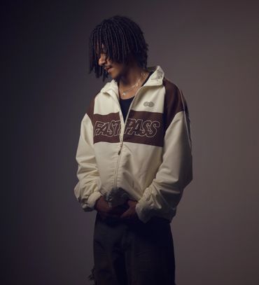 Man with dreadlocks wearing a white and brown jacket that says FASTPASS.